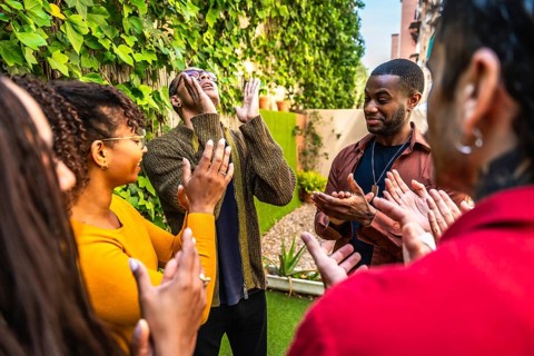 Diverse adults forming a support circle, clapping for one individual, expressing community,