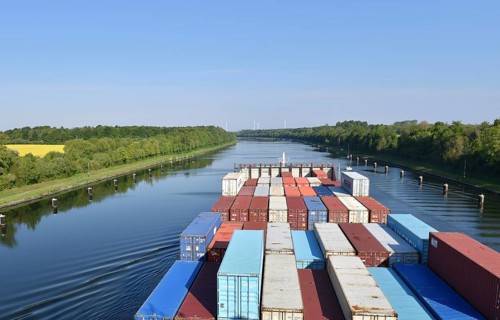 Large container ship sails along a quiet river surrounded by forest, container ship sails through