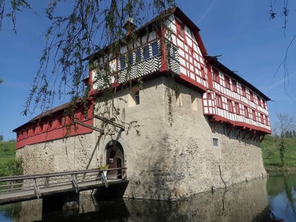 Medieval castle with half-timbered walls, surrounded by water under clear blue skies, Hagenwil,