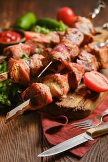 Grilled shish kebabs on a wooden board. The dish includes tender meat, fresh tomatoes, and green