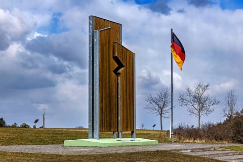 Wooden sculpture and German flag on a field under a dramatic sky, The Point Alpha memorial between