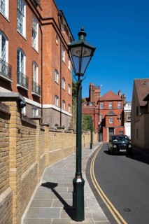 London taxi drives through narrow street lined with historic brick buildings, a street lamp and a