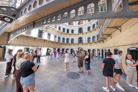 Group of people tour the circular courtyard of a historic building with lattice levels, Kilmainham