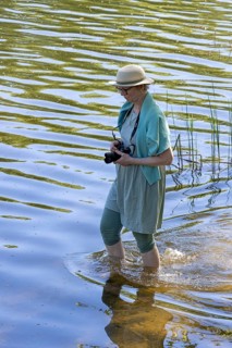 Woman with camera wading through Huwenowsee, Meseberg, Brandenburg, Germany