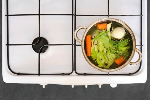 The process of cooking vegetable broth. A pot on a stove with celery, carrot, onion, and other