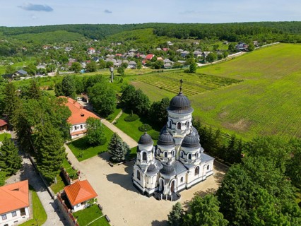 Orthodox church with several domes in a green rural setting under blue sky, aerial view, Capriana