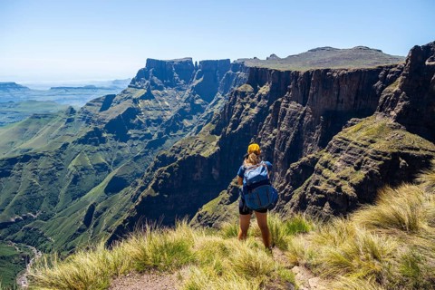 Young hiker looking at the impressive mountains and cliffs of the Drakensberg Mountains, hiking