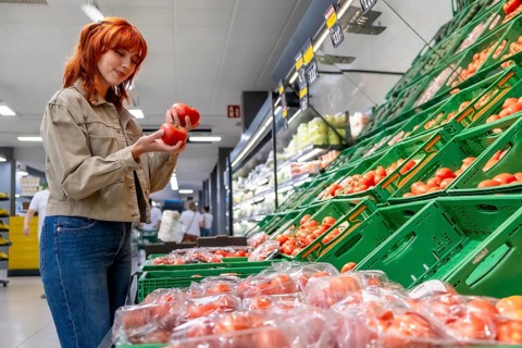 Woman with red hair carefully selecting ripe, organic tomatoes from a display bin, promoting