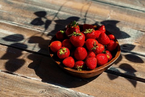 Bowl with ripe strawberries on wooden country table. Bright red fruit displays natural shine.