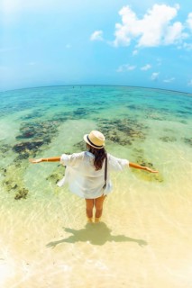 Young carefree woman wear straw hat stands arms wide open hug ocean in shallow, crystal-clear