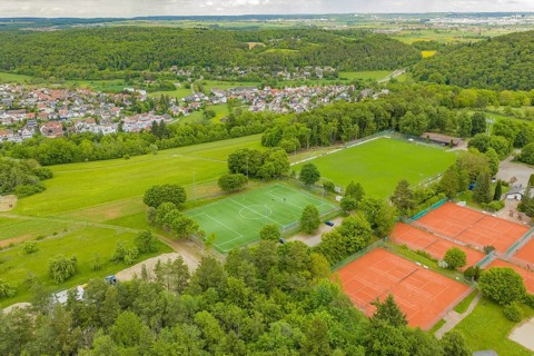 Aerial view of a sports complex with a green soccer field and several red tennis courts, surrounded