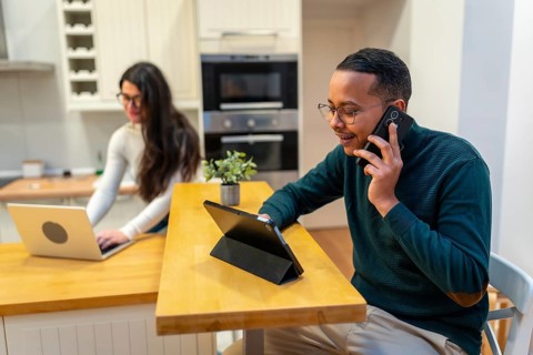 Happy black man talking on smartphone and looking at digital tablet while young woman works on