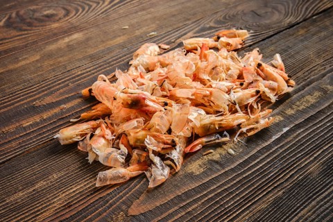 Shrimp shells are piled on a clean wooden table. They come from a recent seafood meal preparation.