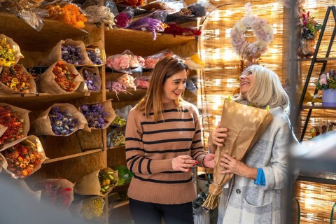 Florist smiling while assisting an older female customer picking out a wrapped dried flower