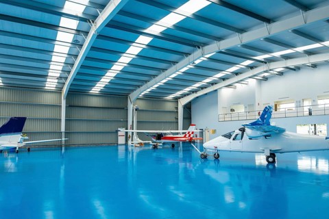 Modern aviation hangar featuring several small private light aircraft parked on a clean blue epoxy