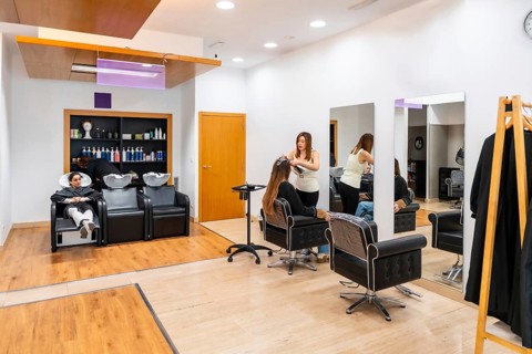 Hairdresser applying hair product to a client sitting in a chair while another client has her hair