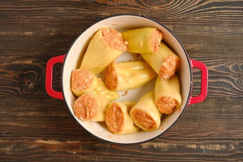 Top view of bell peppers filled with meat and rice in red cast-iron pot on wooden table. This dish