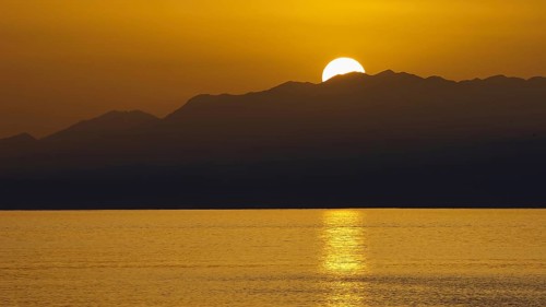 The sun sets behind the mountains and illuminates the sea golden, Matala, South Coast, Crete, Greek