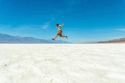 Man jumping joyfully across vast white salt flats of badwater basin, death valley, silhouetted