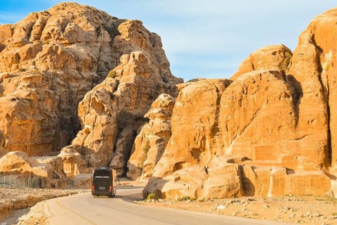Black passenger coach bus driving asphalt road winding through sandstone rock mountains canyon