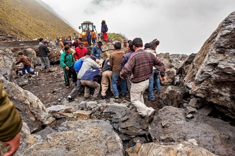Group of people move a rock on a foggy mountain road with a tractor in the background, rockslide on