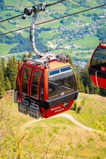Red cable car cabin floating over green landscape with a view of a village in the distance,