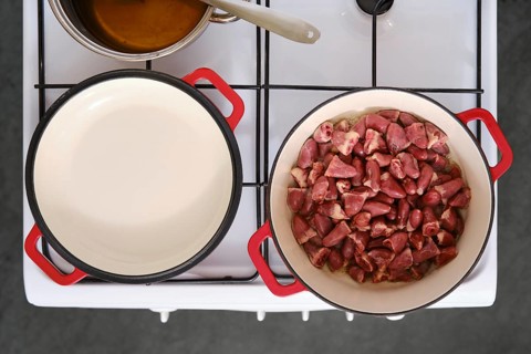 A stove is set up in a kitchen with two pots. One pot has raw chicken hearts, while the other pot