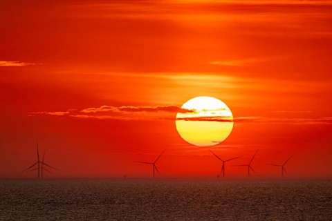 Dramatic sunset over the sea, wind turbines and wind turbines on the horizon, streaks of clouds,