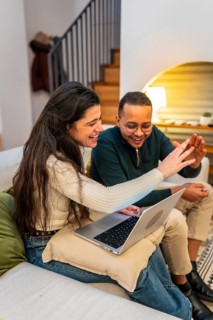 Happy multiethnic couple laughing and bonding over a cozy laptop video call while relaxing on their