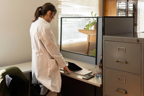 Young female scientist in white lab coat standing and closing a laptop on a bright office desk