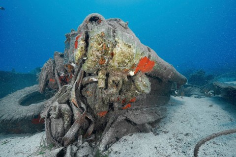Close-up of the engine of a corroded wreck on the seabed, covered with paint residue and sand,
