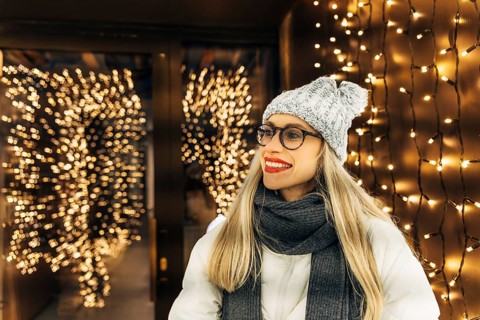 Young woman in winter clothing with festive lights in background. A woman wearing a gray knit hat,
