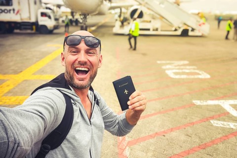 Excited young man traveler taking selfie airplane tarmac holding passport travel document departure