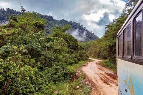 A bus travels along a dirt road surrounded by misty rainforest mountains, bus ride from La Paz