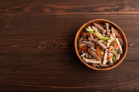 Meat salad with beef and vegetables in wooden bowl on brown wooden background. top view, flat lay,