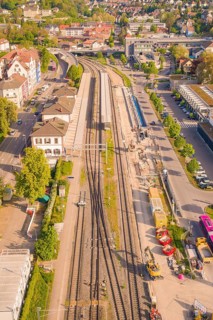 Bahnhofstraße with tracks and construction, surrounded by buildings and green trees in sunny
