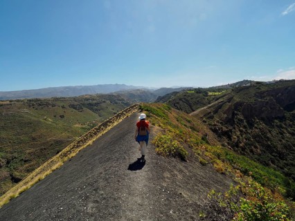 Person hiking on a narrow ridge with a view of a volcanic crater, Caldera de Bandama Natural Park,