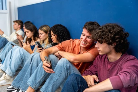 Diverse group of young students sitting in a row, individually focused on their mobile phones while