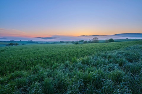 Dawn over a wide field with rolling hills in the background and a calm blue sky, Mönchberg,