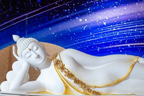 A reclining Buddha, crafted from white material, rests in the classic Parinirvana pose, golden