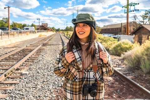 Young female tourist smiling and looking away, wearing a hat, plaid shirt, and backpack with a