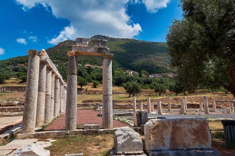 Ancient columns with stone formations against green hill and blue sky, ancient site, archaeological