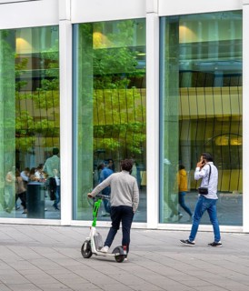 Young man with an electric scooter standing in front of the entrance to the One office building in