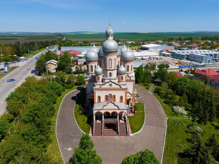 Orthodox church with large silver domes surrounded by fields and buildings in a rural area, aerial
