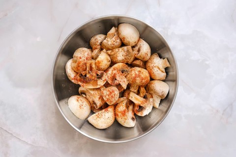 Top view of fresh champignon mushrooms in a round metal bowl. They are covered with a layer of