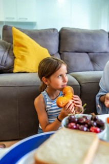 Young granddaughter happily eating a shaped pastry during a snack time at home, sharing a moment
