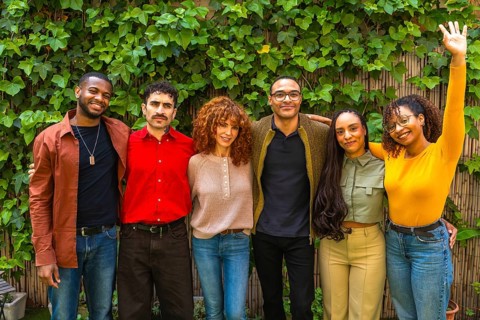 Diverse group of smiling adults supporting each other, standing together outside against a green