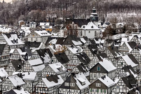 Snow-covered half-timbered houses and a church in a village in front of a wooded hill, The historic