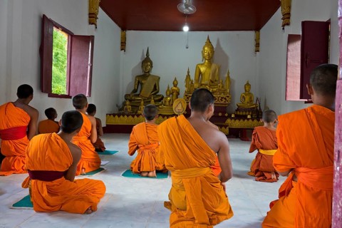 Laotian novices in orange robes in front of a golden Buddha figure in a newly built Buddhist
