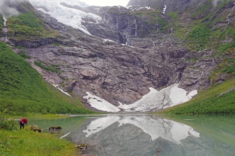 A calm lake with mountains and snowy rocks, reflecting the surrounding landscape, glaciers, climate